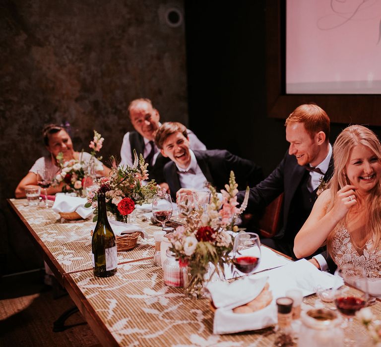 Bride in Lila Gown by Alexandra Grecco with Fitted Silk Crepe Skirt and Sheer Italian Tulle Bodice Covered in Floral Lace Applique | Groom in Black Three-Piece Suit from Hackett with Burgundy Bow Tie from Zara | Pink, Red and White Flowers in Jam Jars | Wedding Reception at Brody Studios, Budapest, Hungary | Budapest Wedding with Giant Bridal Bouquet, Tuk Tuks and Cadillac | Jágity Fanni Fotográfus