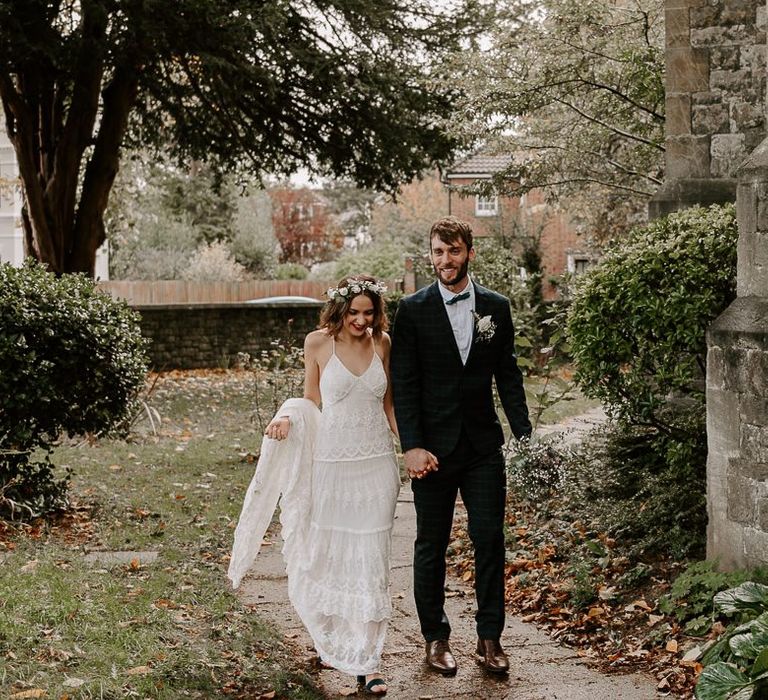 Bride wearing a Spell And The Gypsy boho dress with white floral crown and red lip plus groom in checked suit and bow tie