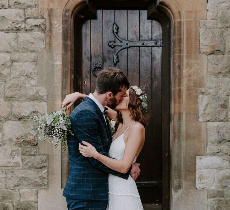 Bride and groom embrace wearing boho style dress with white floral bouquet and hair crown