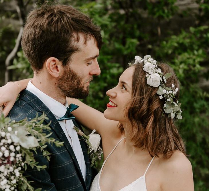 Bride wearing white floral hair crown with red lip and groom wearing checked suit with green bow tie