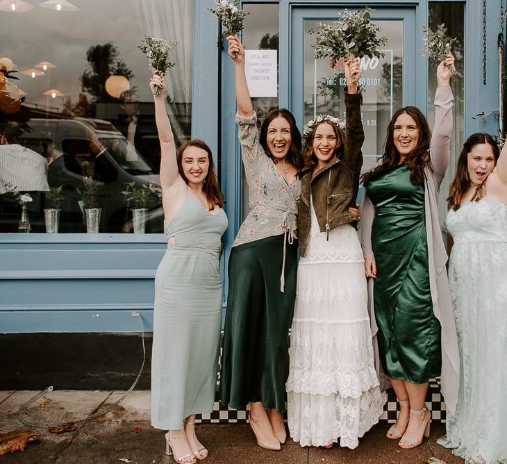 Bride wearing beautifully laced Spell And The Gypsy dress with bridesmaids wearing green dresses plus white floral bouquets