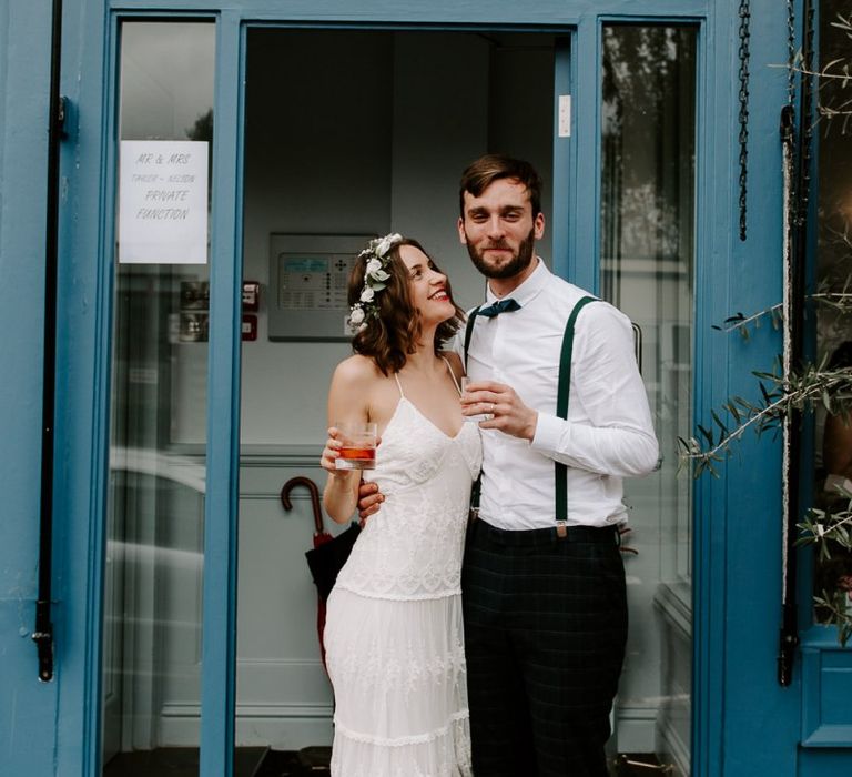 Bride wearing laced boho Spell And The Gypsy dress with a white floral crown plus groom wearing green satin bow tie