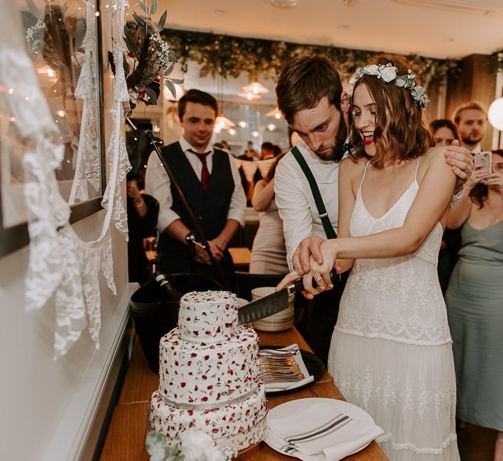 Bride wearing Spell And The Gypsy dress cutting the homemade dried flower cake with her groom