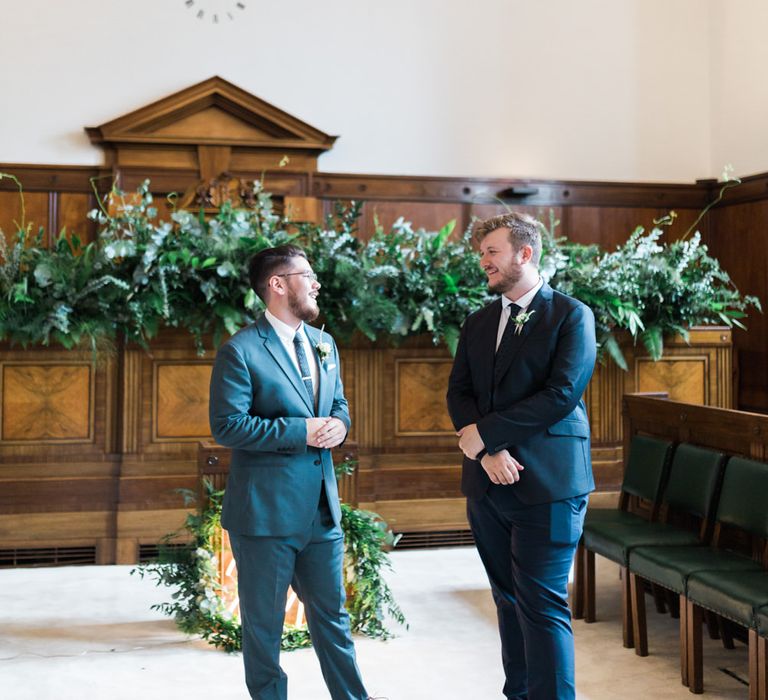 Groom in Blue Reiss Suit with Brown Grenson Shoes | Best Man in Navy Suit with Le Colonel Moutarde Tie | Neon You &amp; Me Sign at Altar | Town Hall Hotel Bethnal Green | Neon Sign and Marine Green Rewritten Bridesmaids Dresses with Lace Cape Grace Loves Lace Gown | Alain Mbouche Photography