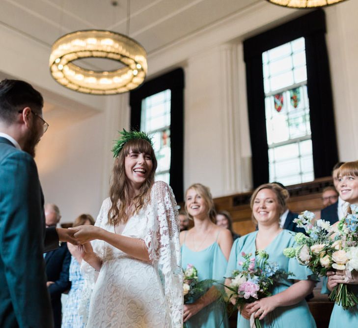 Bride in Grace Loves Lace Verdelle Dress with V-Neck, Low Square Back, Mid-Thigh Front Split and Lace Cape | Foliage Hair Crown | Groom in Blue Reiss Suit with Brown Grenson Shoes | Bridesmaids in Mismatched Marine Green Rewritten Dresses | Town Hall Hotel Bethnal Green | Neon Sign and Marine Green Rewritten Bridesmaids Dresses with Lace Cape Grace Loves Lace Gown | Alain Mbouche Photography