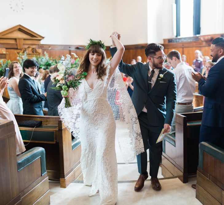 Bride in Grace Loves Lace Verdelle Dress with V-Neck, Low Square Back, Mid-Thigh Front Split and Lace Cape | Foliage Hair Crown | Pastel Bridal Bouquet | Groom in Blue Reiss Suit with Brown Grenson Shoes | Town Hall Hotel Bethnal Green | Neon Sign and Marine Green Rewritten Bridesmaids Dresses with Lace Cape Grace Loves Lace Gown | Alain Mbouche Photography