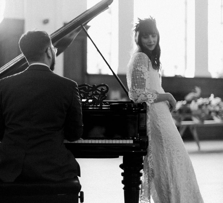 Bride in Grace Loves Lace Verdelle Dress with V-Neck, Low Square Back, Mid-Thigh Front Split and Lace Cape | Foliage Hair Crown | Gold Flat Gianvito Rossi Sandals | Groom in Blue Reiss Suit with Brown Grenson Shoes | Steinway Grand Piano | Neon Sign and Marine Green Rewritten Bridesmaids Dresses with Lace Cape Grace Loves Lace Gown | Alain Mbouche Photography