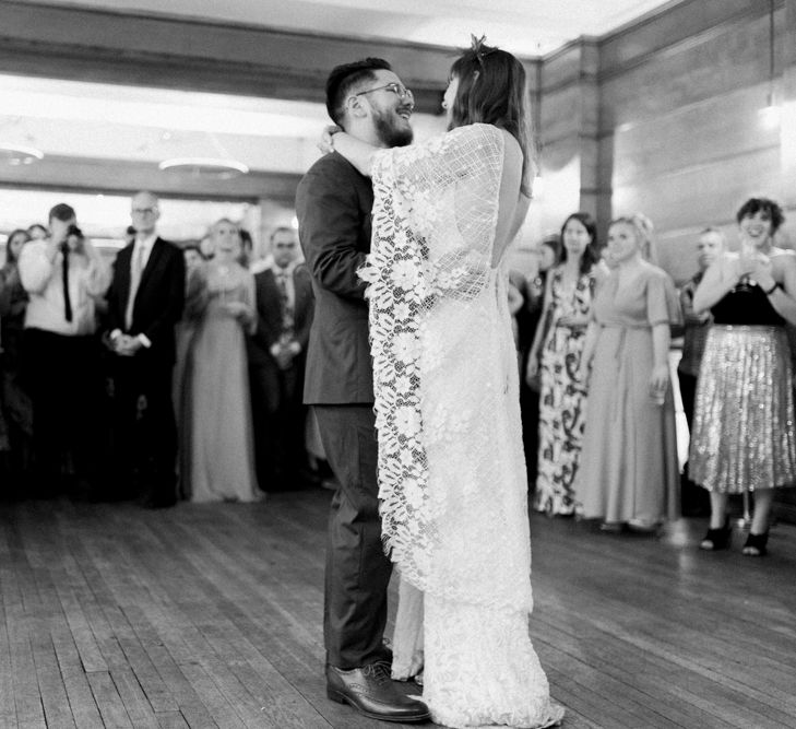 Bride in Grace Loves Lace Verdelle Dress with V-Neck, Low Square Back, Mid-Thigh Front Split and Lace Cape | Foliage Hair Crown | Groom in Blue Reiss Suit with Brown Grenson Shoes | First Dance at Town Hall Hotel Bethnal Green | Neon Sign and Marine Green Rewritten Bridesmaids Dresses with Lace Cape Grace Loves Lace Gown | Alain Mbouche Photography