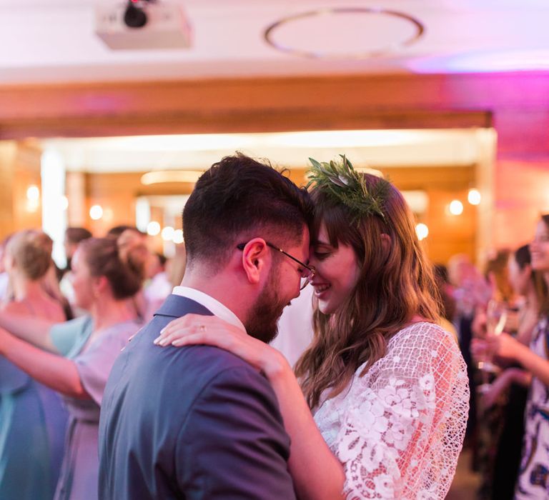 Bride in Grace Loves Lace Verdelle Dress with V-Neck, Low Square Back, Mid-Thigh Front Split and Lace Cape | Foliage Hair Crown | Groom in Blue Reiss Suit with Brown Grenson Shoes | First Dance at Town Hall Hotel Bethnal Green | Neon Sign and Marine Green Rewritten Bridesmaids Dresses with Lace Cape Grace Loves Lace Gown | Alain Mbouche Photography