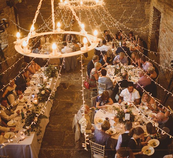 Wedding guests enjoy dinner under fairy lights and chandelier