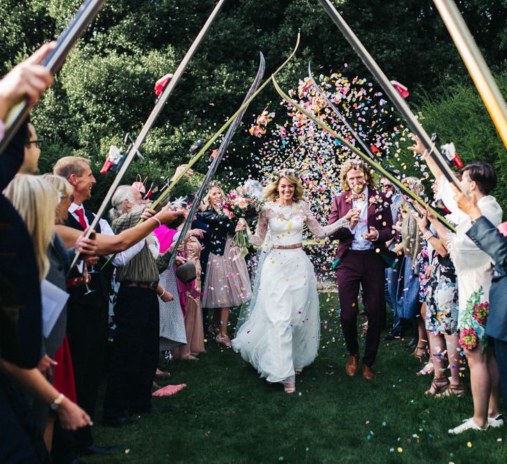 Confetti Moment with Bride in Separates and Flower Crown and Groom in Burgundy Suit Walking Under a Skies Tunnel