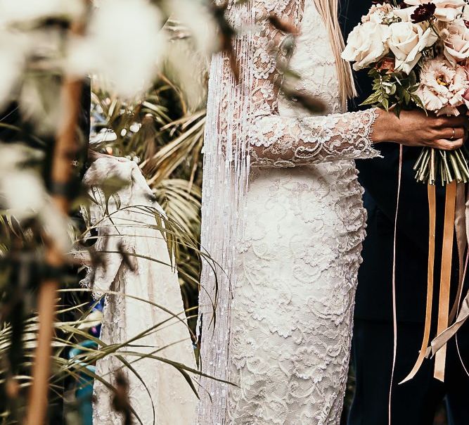 Lace and beaded boho bridal dress with tassel detailing and a pink bouquet