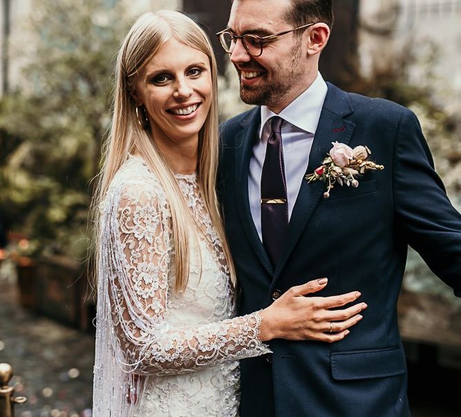 Bride wearing a lace and beaded boho style dress embraces with groom in Ted Baker suit