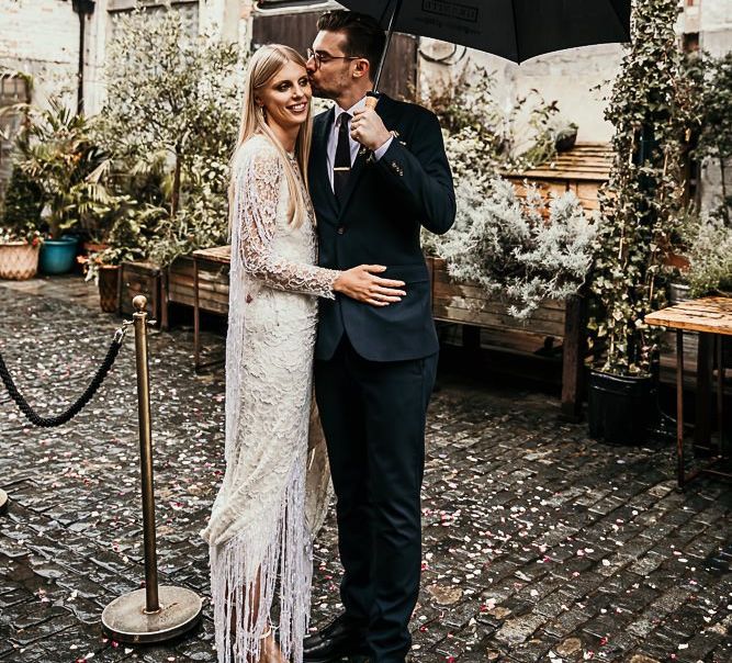 Bride wearing a lace and beaded boho style dress embraces with groom in Ted Baker suit