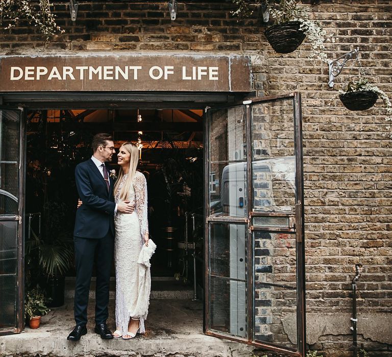 Bride wearing a lace and beaded boho style dress embraces with groom in Ted Baker suit at Clapton Country Club wedding