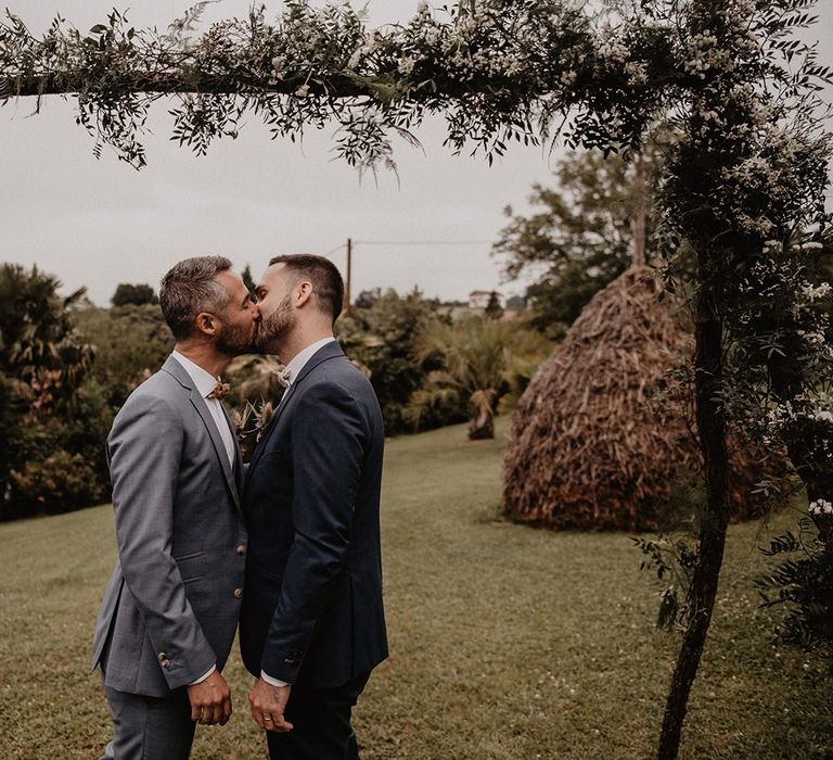 Grooms kiss under wooden arch