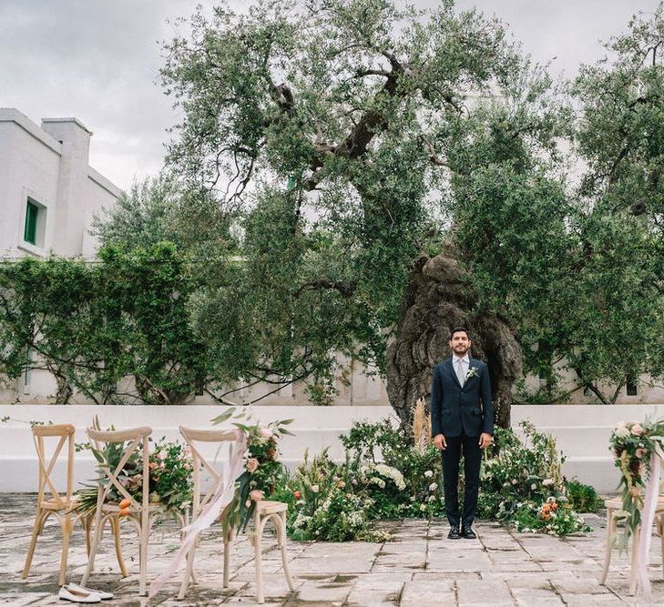 Groom in Navy Suit at the Altar Surrounded by Foliage and Flower Floral Arrangements