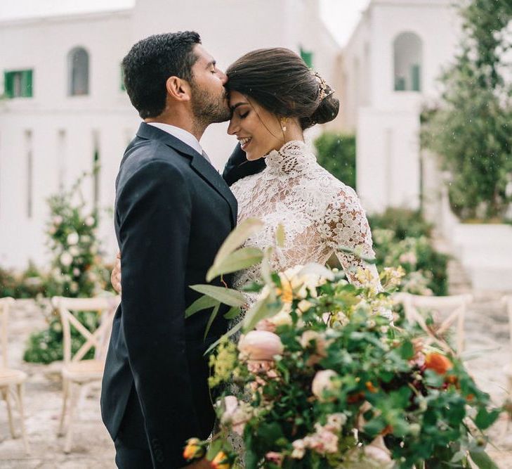 Groom in Navy Suit Kissing His Brides Head at Their Wedding Ceremony