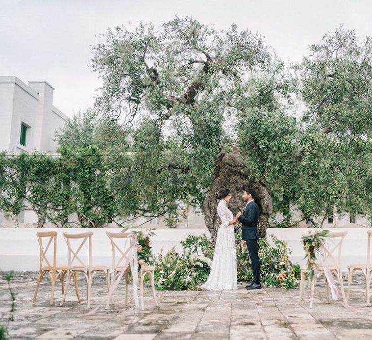 Bride in Lace Wedding Dress and Groom in Navy Suit Standing at the Outdoor Ceremony Altar