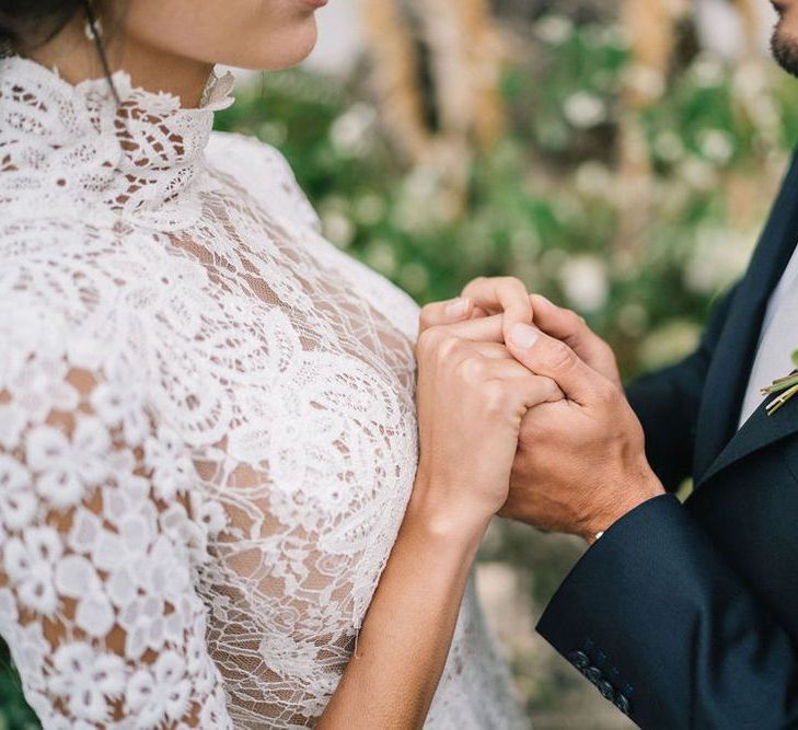 Bride in Lace Wedding Dress and Groom in Navy Suit Holding Hands