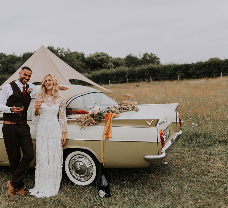 Boho Bride and Groom Standing Next to a Vintage Wedding Car