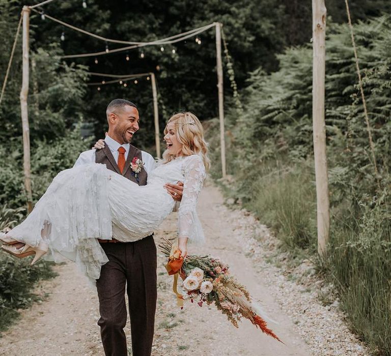 Groom in Wool Suit Picking Up His Bride in a Lace Wedding Dress