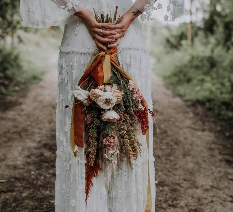 Boho Bride in a Lace Wedding Dress Holding Her Natural Bouquet Behind Her Back