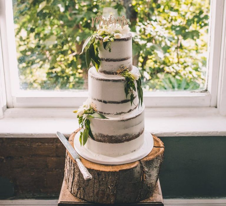 Semi-naked cake with white floral decoration on a tree trunk stand