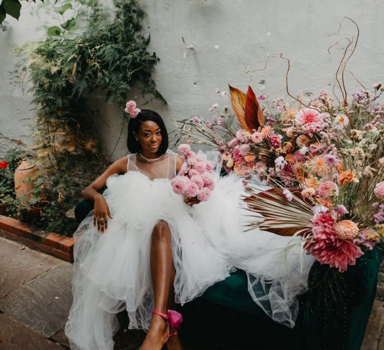 Bride in tulle wedding dress sitting on a flower filled sofa at Secret Garden Kent