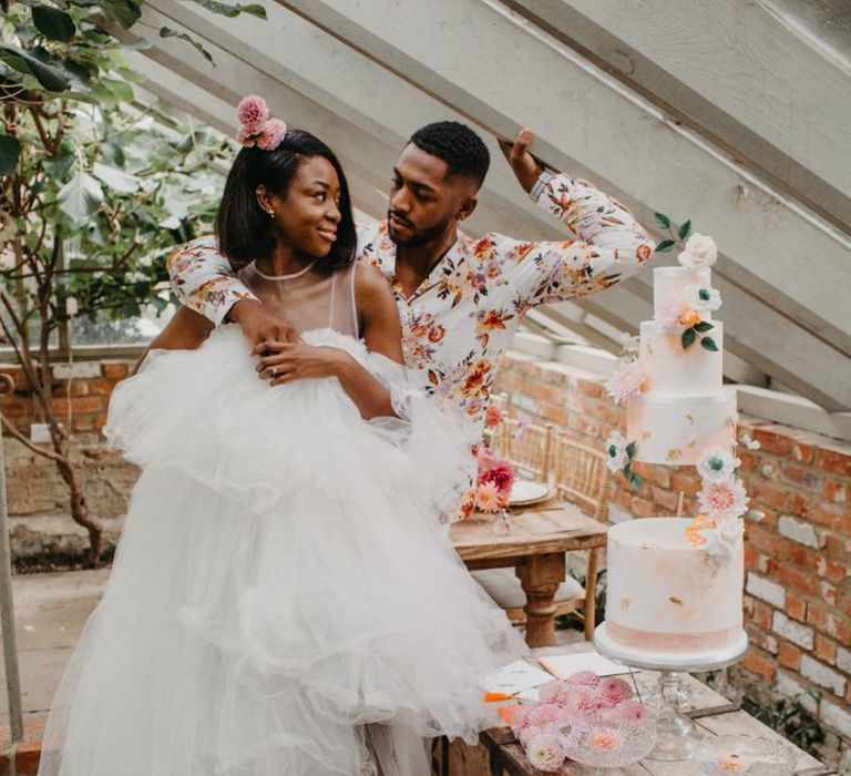 Bride in tulle wedding dress and groom in floral shirt cutting the wedding cake at tropical wedding