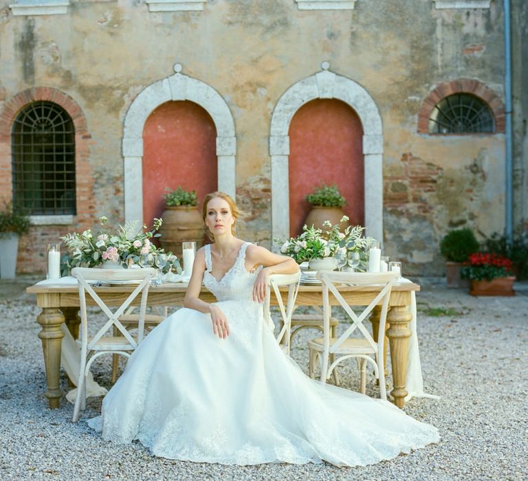 Bride in Lace Sorrisi di Gioia Wedding Dress Sitting in Front of a Rustic Tablescape