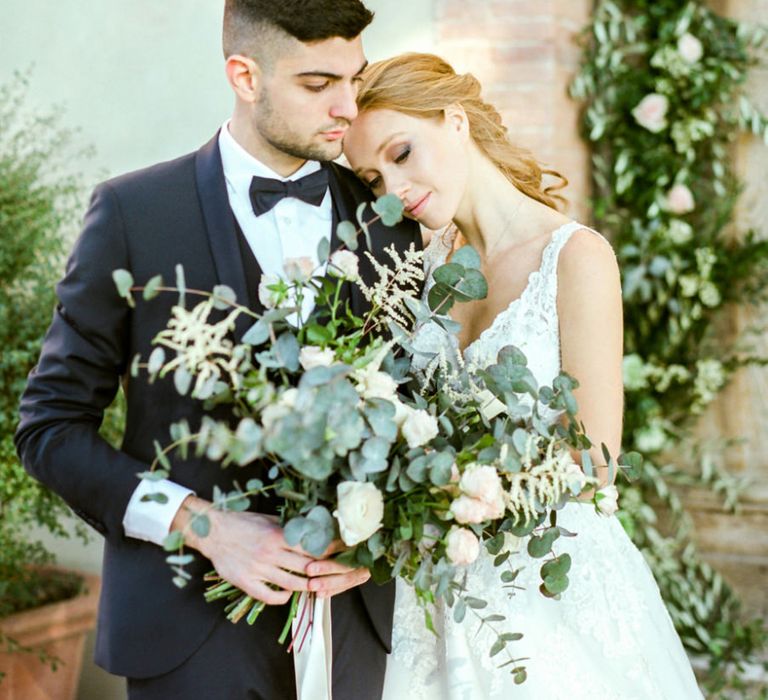 Bride in Lace Sorrisi di Gioia Wedding Dress and Groom in Black Tie Suit Holding an Oversized Wedding Bouquet