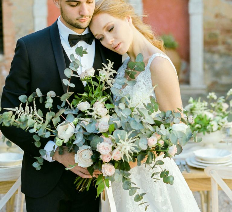 Bride in Lace Sorrisi di Gioia Wedding Dress and Groom in Black Tie Suit Holding an Oversized Wedding Bouquet