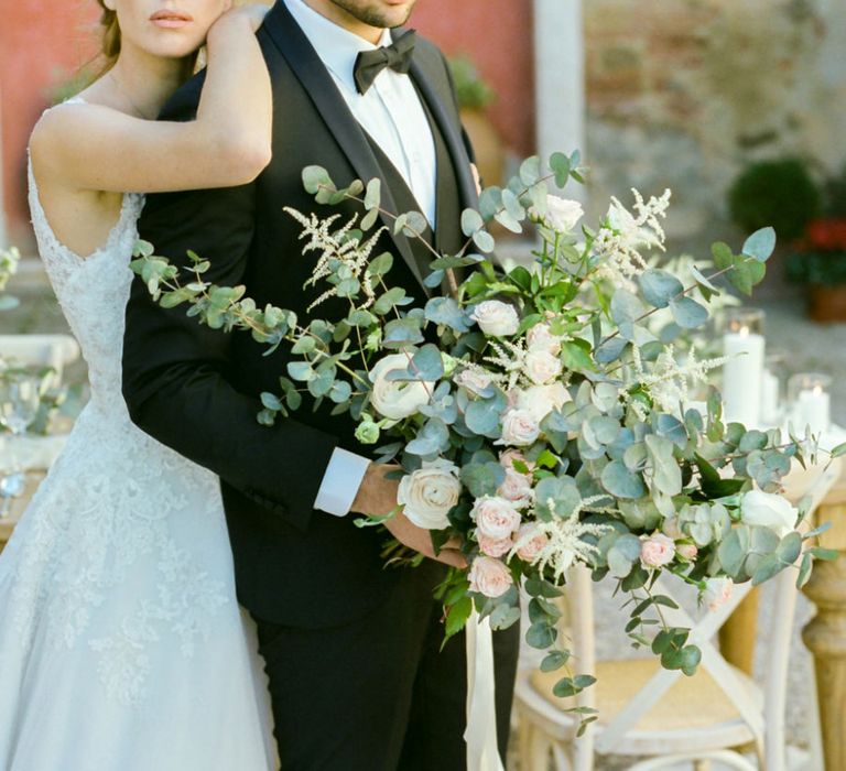 Bride with Natural Makeup in Lace Sorrisi di Gioia Wedding Dress and Groom in Black Tie Suit Holding an Oversized Wedding Bouquet