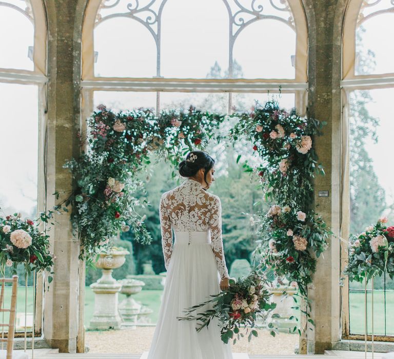 Bride at the Floral Arch Altar in Lace Bodice Suzanne Neville Wedding Dress | Blush &amp; Burgundy Floral Fairytale Wedding Inspiration at Grittleton House Planned &amp; Styled by Jennifer Louise Weddings | Katherine Yiannaki Photography