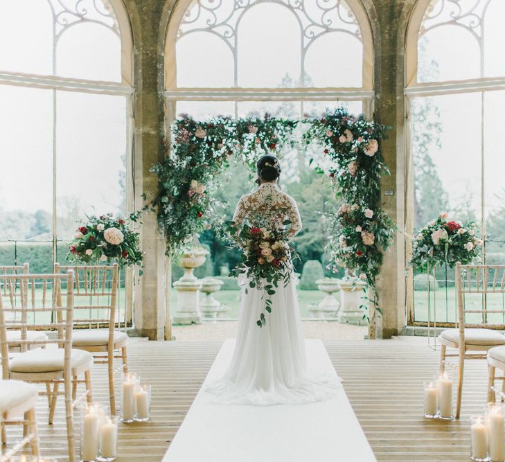 Bride at the Floral Arch Altar in Lace Bodice Suzanne Neville Wedding Dress | Blush &amp; Burgundy Floral Fairytale Wedding Inspiration at Grittleton House Planned &amp; Styled by Jennifer Louise Weddings | Katherine Yiannaki Photography