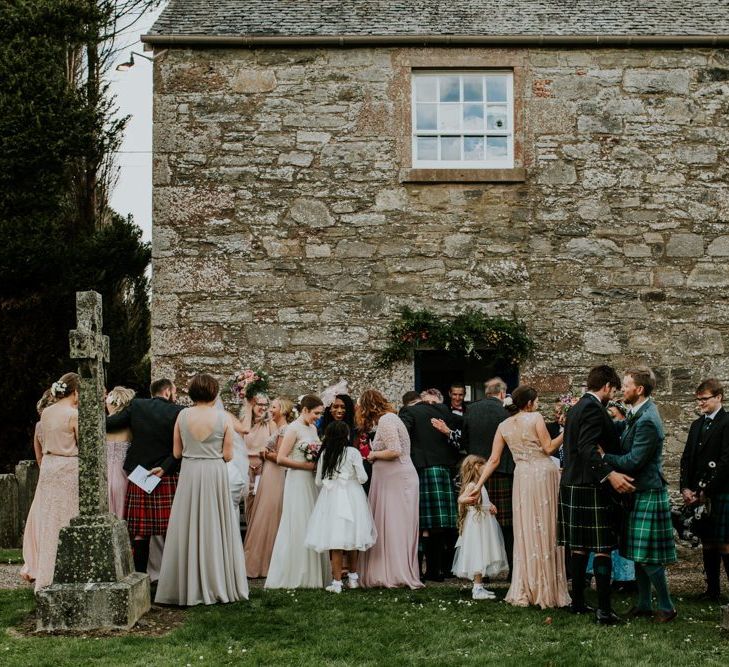 Wedding party gathers outside church for wedding with hanging flower decor