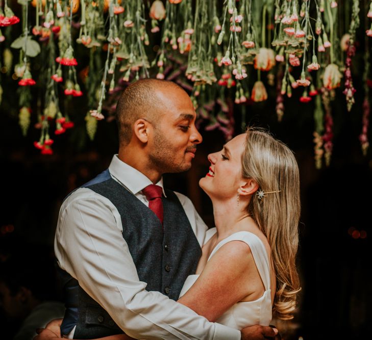 Bride and groom underneath hanging flowers