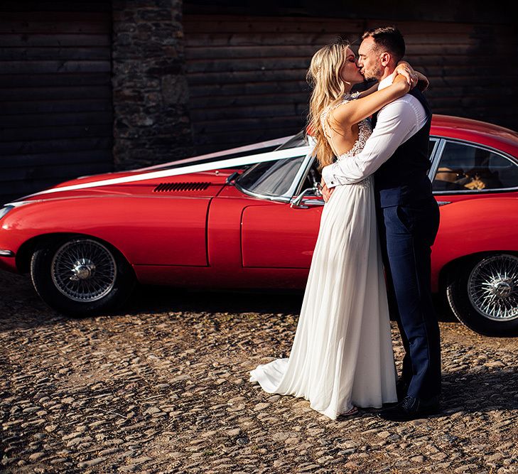 Bride and groom embracing in front of a red sports car