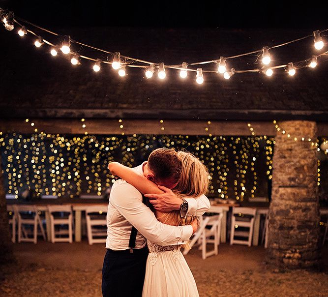 Bride and groom embracing under festoon lights