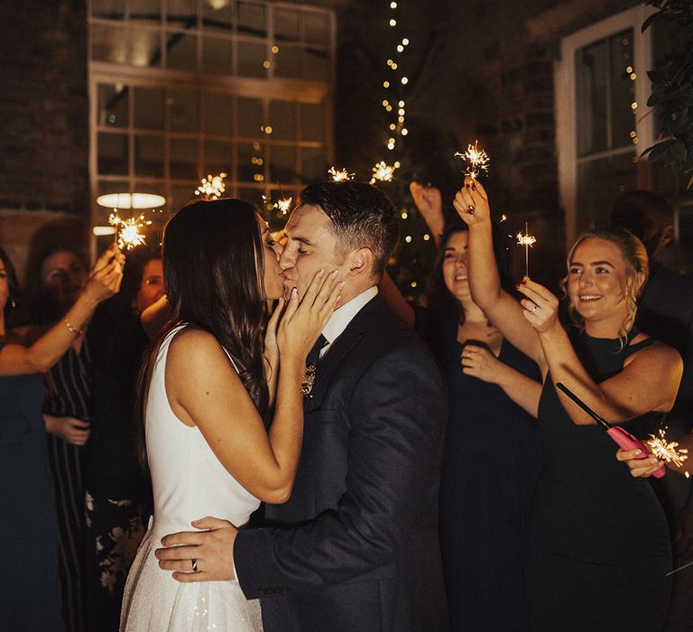 Bride in Charlie Brear Wedding Dress and Groom in Next Suit Kissing During Sparkler Moment