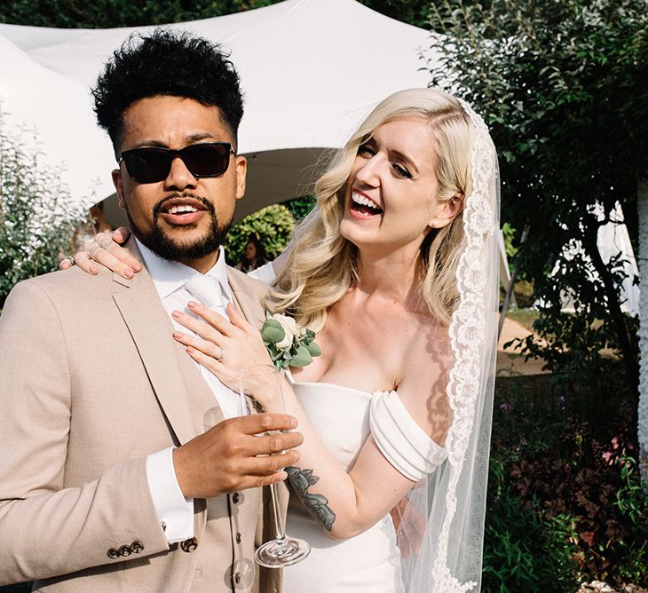 Cool Groom in Sunglasses and Beige Moss Bros. Suit and Bride in Bardot Pronovias Wedding Dress