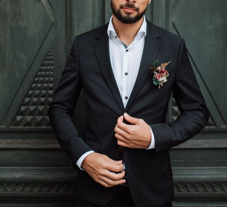 Groom in Black Suit and White Skirt with Red Buttonhole