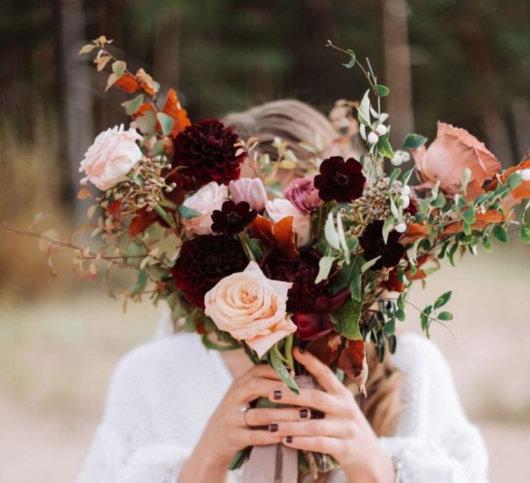 Bride in Wool Coverup Holding a Muted Pink and Red Wedding Bouquet Tied with Ribbon