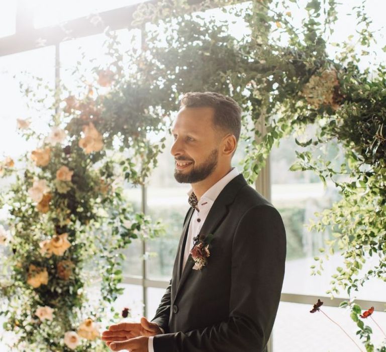 Groom in Black Suit Clapping at the Floral Moon Gate Altar