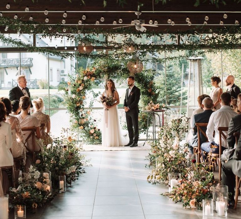 Bride and Groom Standing at the Floral Moon Gate Altar During the Wedding Ceremony