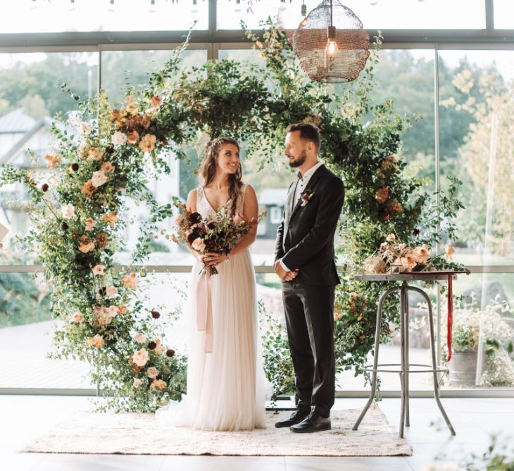 Celebrant Leading the Wedding Ceremony with the Bride and Groom Standing in Front of the Foliage and Flower Filled Moon Gate