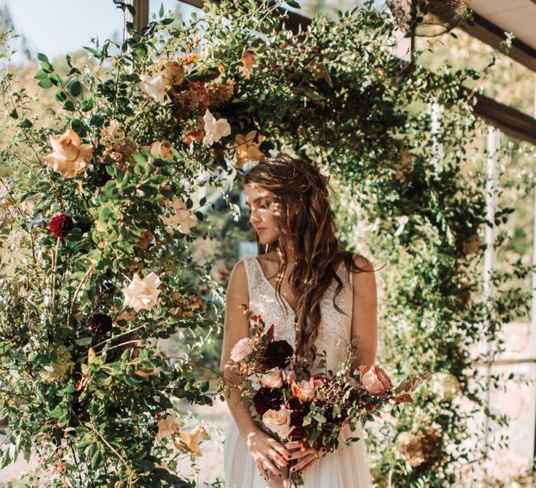 Bride in Fay Katya Katya Wedding Dress Standing in Front of a Floral Moon Gate holding a Bridal Bouquet