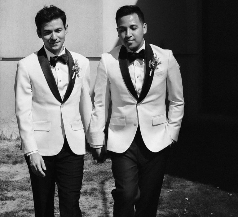 Grooms in white dinner jackets holding hands