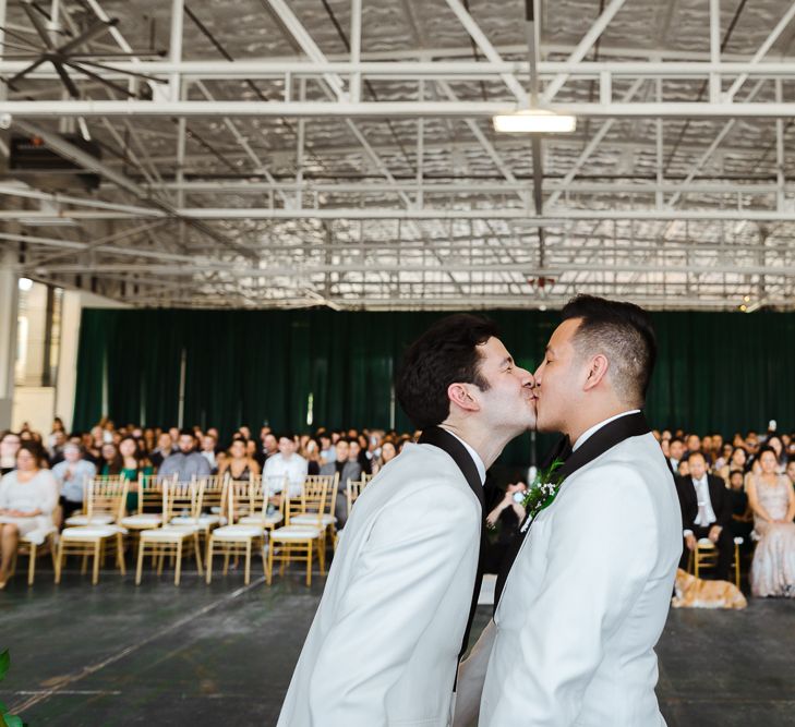 Groom and groom kissing at their industrial wedding ceremony in an airplane hangar